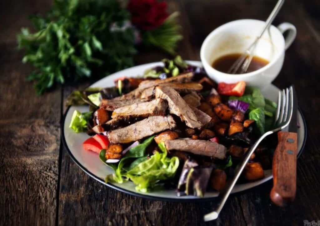 A plate of steak salad with dressing on a wooden table.