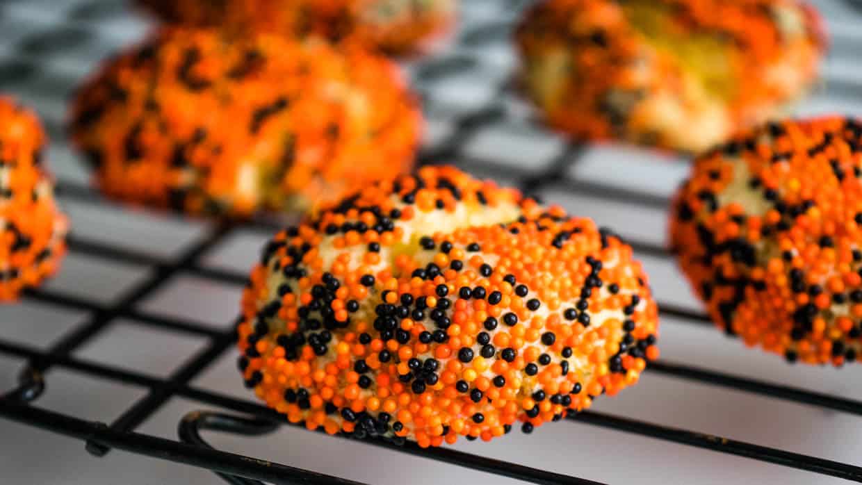 Some orange and black sprinkled cookies on a cooling rack.