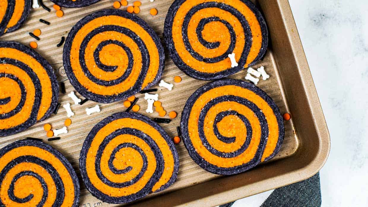 A baking sheet filled with orange and black swirled cookies.