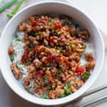 A white bowl with rice and hoisin ground beef and chopsticks on the side.