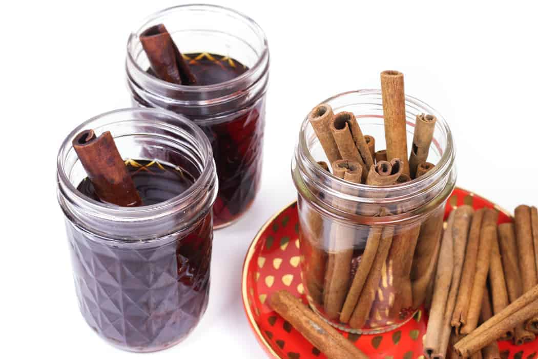 Two jars of cinnamon whiskey with cinnamon sticks on a plate.