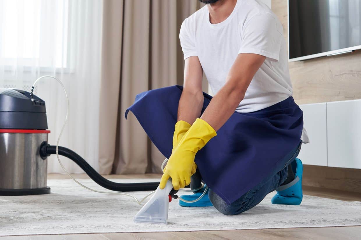 A man cleaning a carpet with a vacuum cleaner.