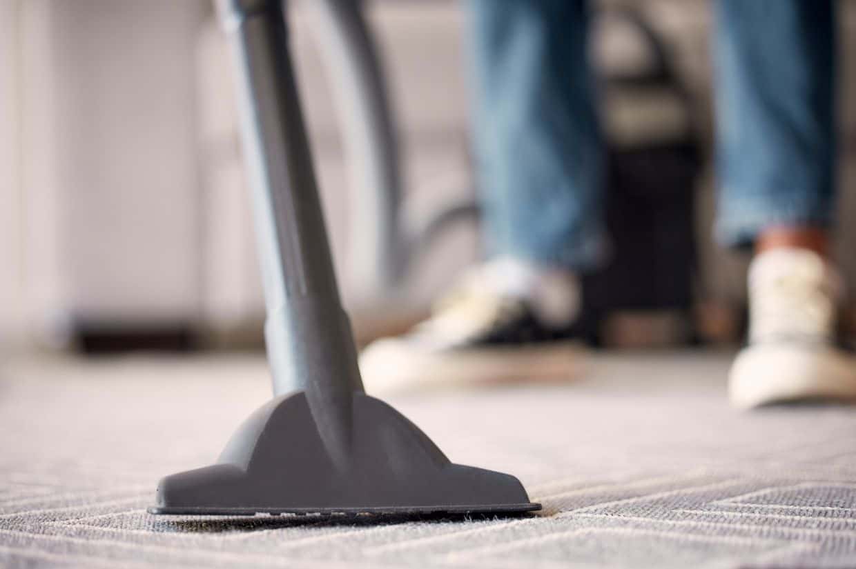 A person cleaning a carpet with a vacuum.