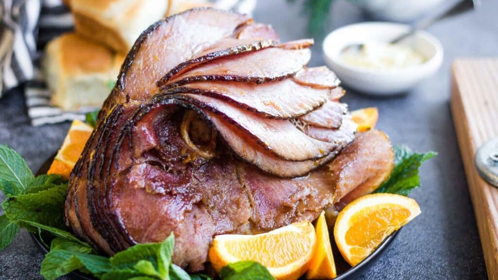 A sliced ham with orange slices and mint leaves on a platter.