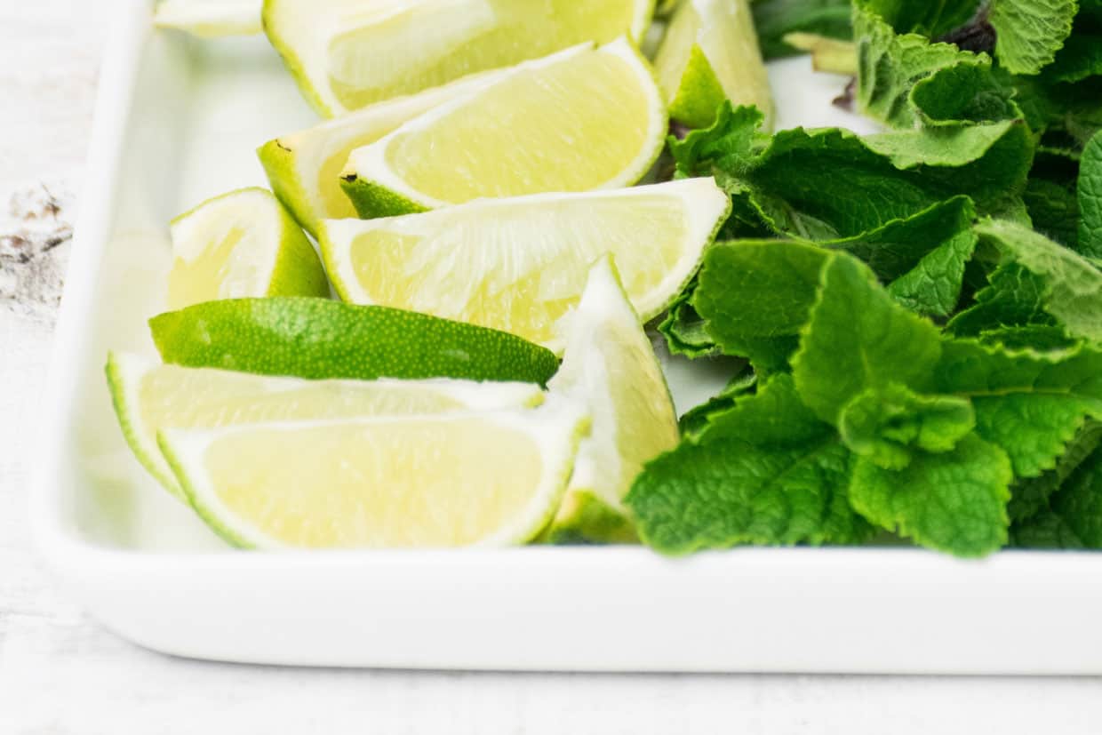 Lime slices and mint leaves on a white plate.