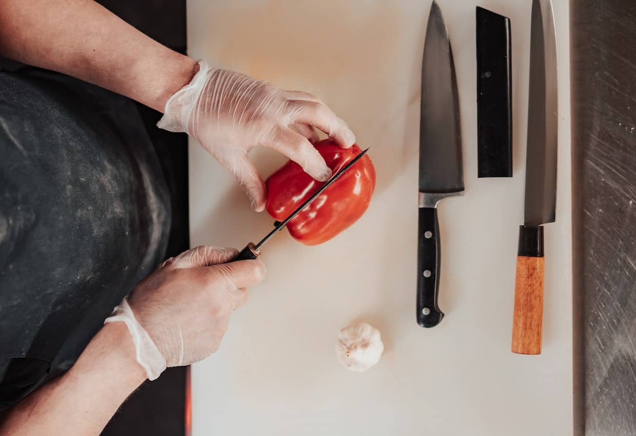 A person cutting a red pepper on a cutting board.