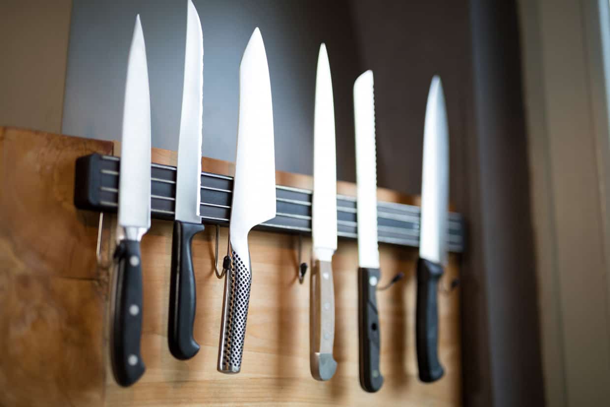 Five knives hanging on a wooden rack.