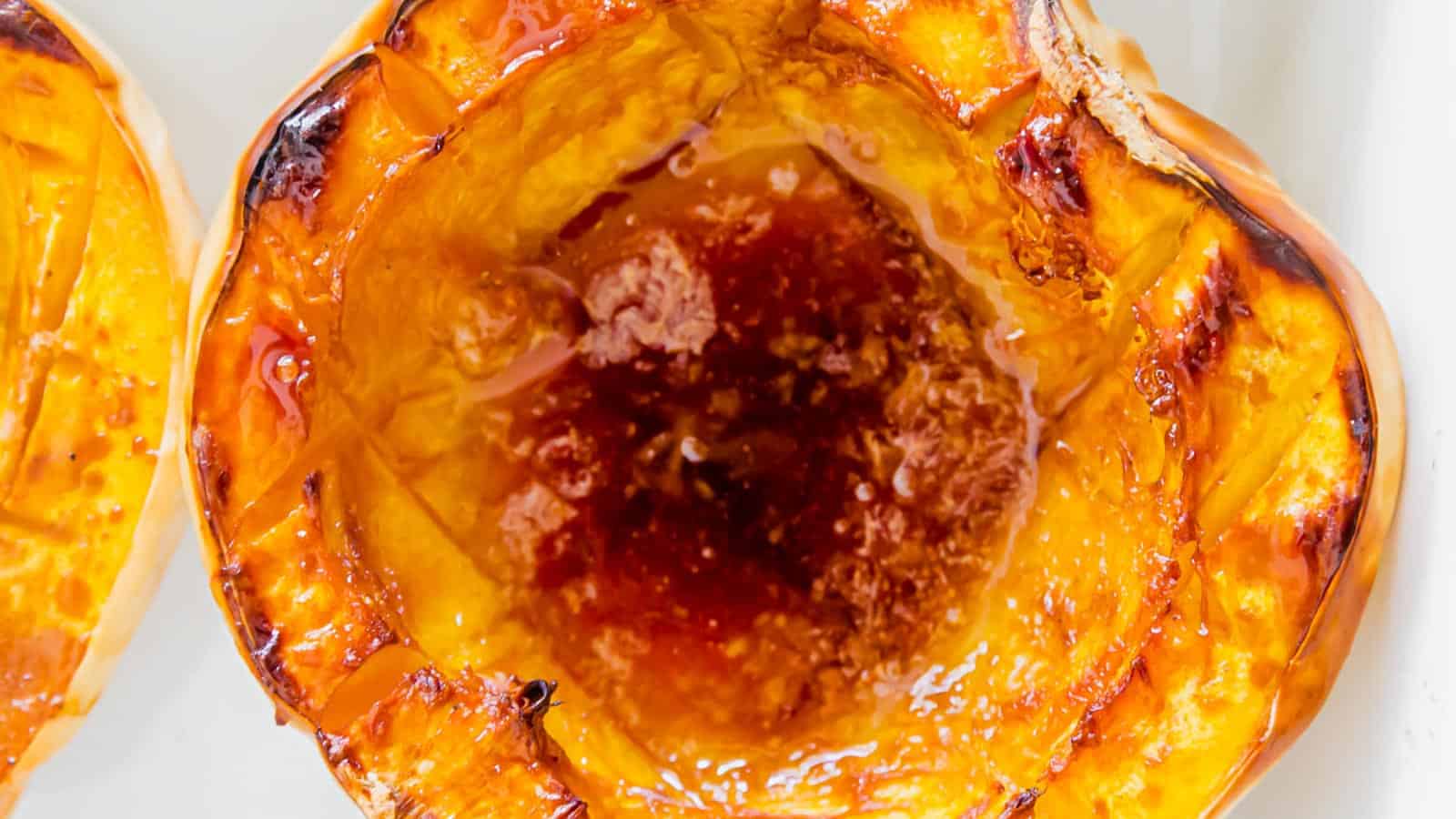 Two halves of a roasted white acorn squash in a white baking dish with maple syrup.