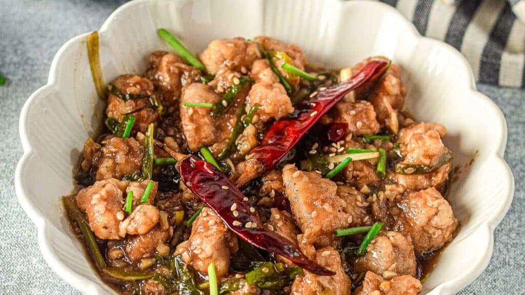 A white bowl with Mongolian chicken studded with dried hot chiles.