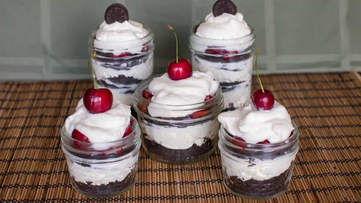 Four mason jars filled with whipped cream, Oreos and cherries.