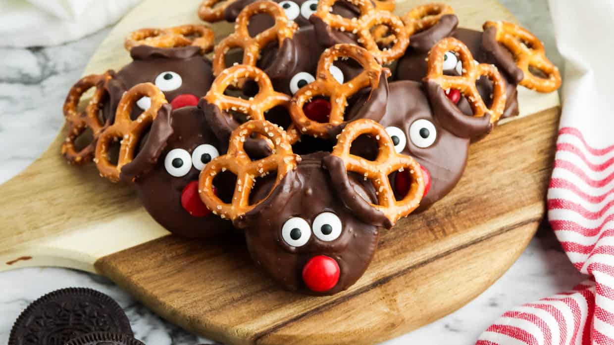 Chocolate reindeer Oreos with pretzels on a cutting board.