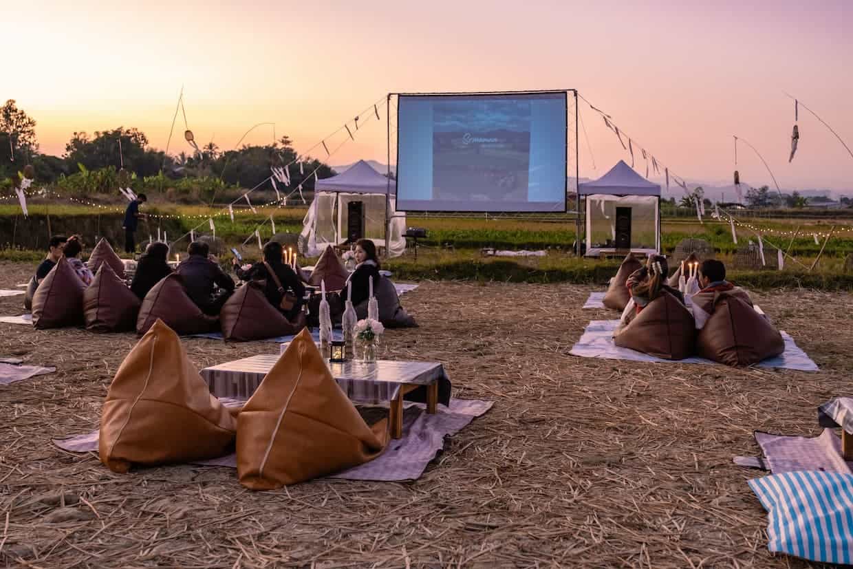 Outdoor cinema setting with pillows and blankets and small tables. 
