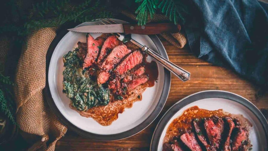 Two plates of steak on a wooden table.