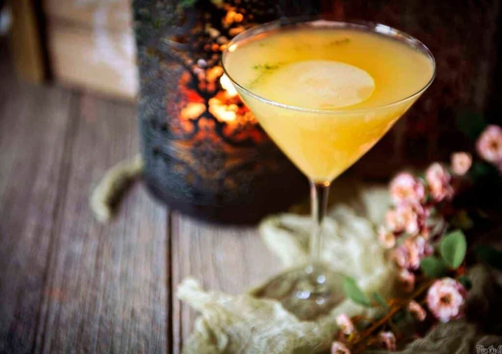 A martini with pear slice and flowers on a wooden table.