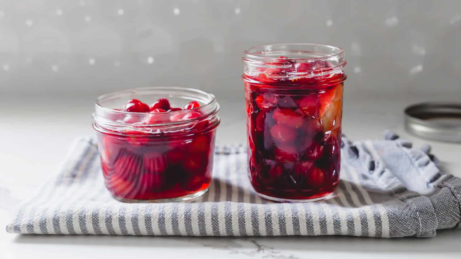 Two jars of pickled cranberries on a kitchen towel.