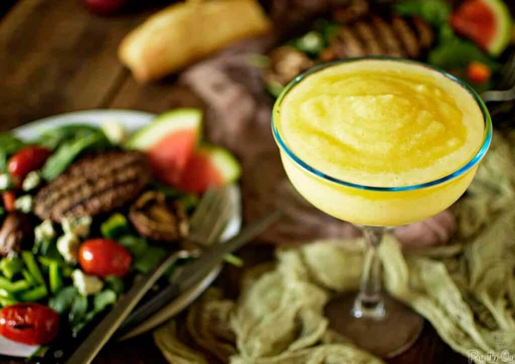 A glass of frozen margarita\ with a salad on it.