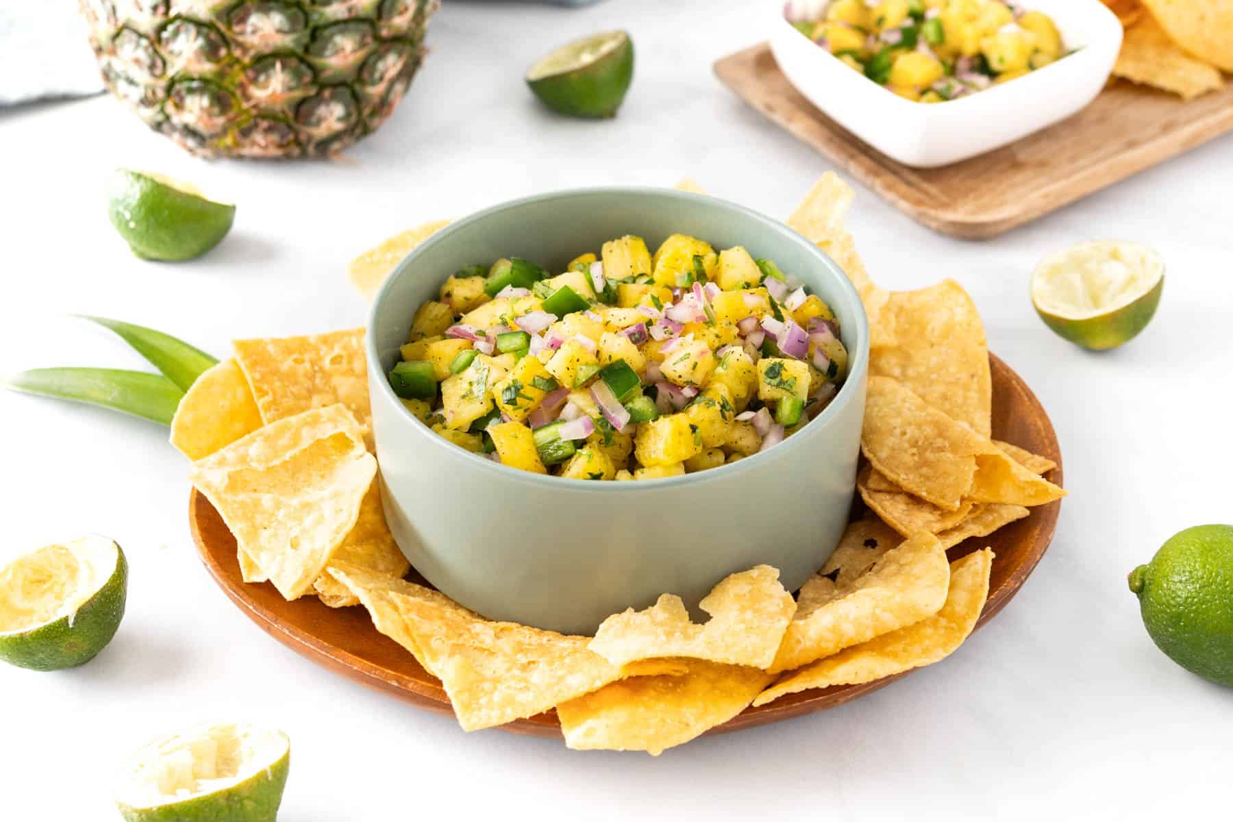 A bowl of pineapple salsa with chips and limes.