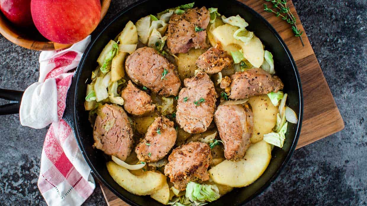 Pork chops with apples and onions in a skillet.