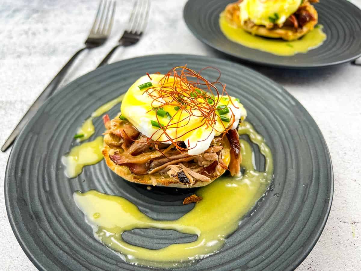Two pulled pork eggs benedict on a plate with sauce.