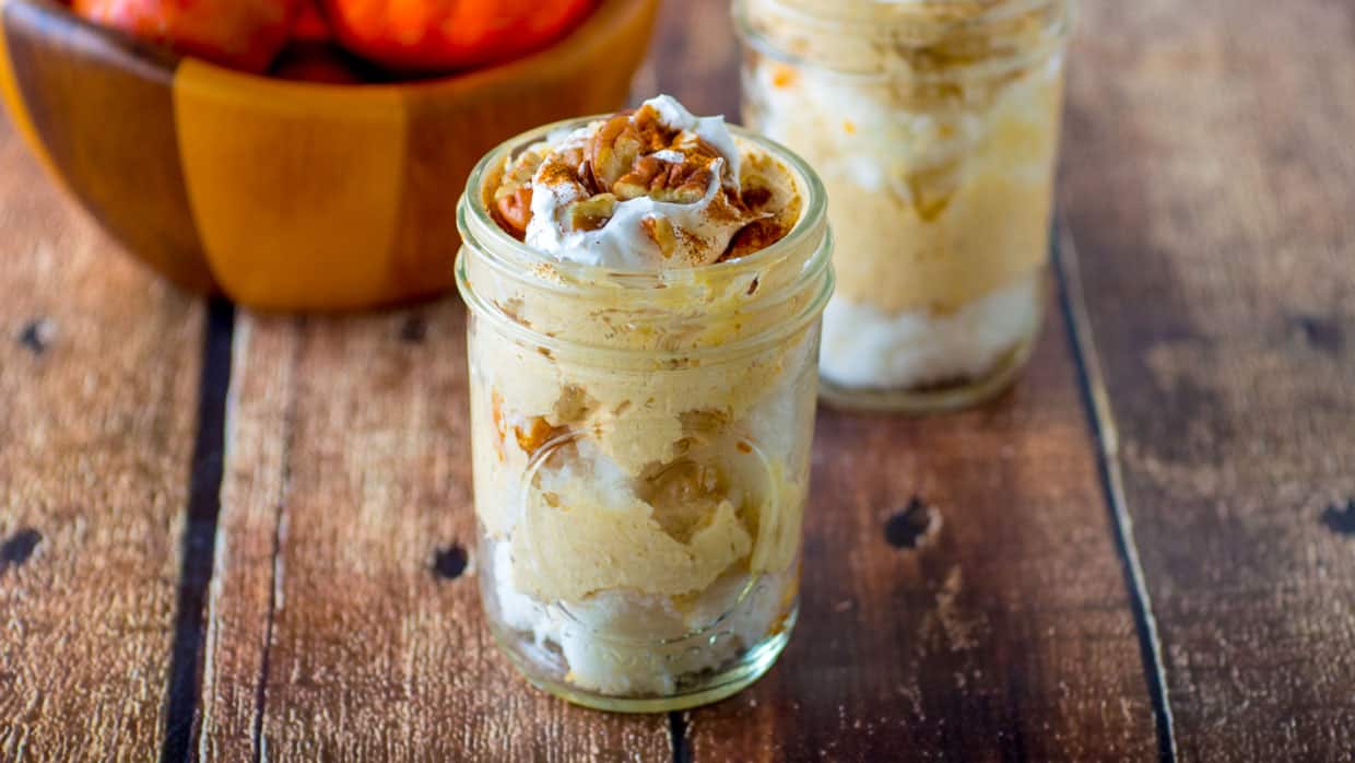 Mason jar with pumpkin cheesecake trifle topped with whipped cream and pecans.