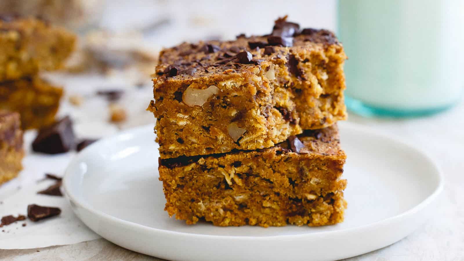 Two stacked pumpkin chocolate chip bars with walnuts on a white plate.