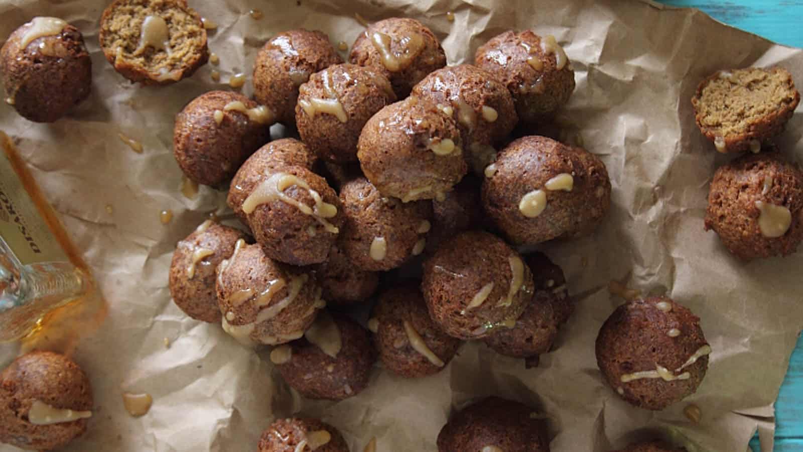 Chocolate pumpkin donut holes on crumbled brown paper drizzled with amaretto glaze.