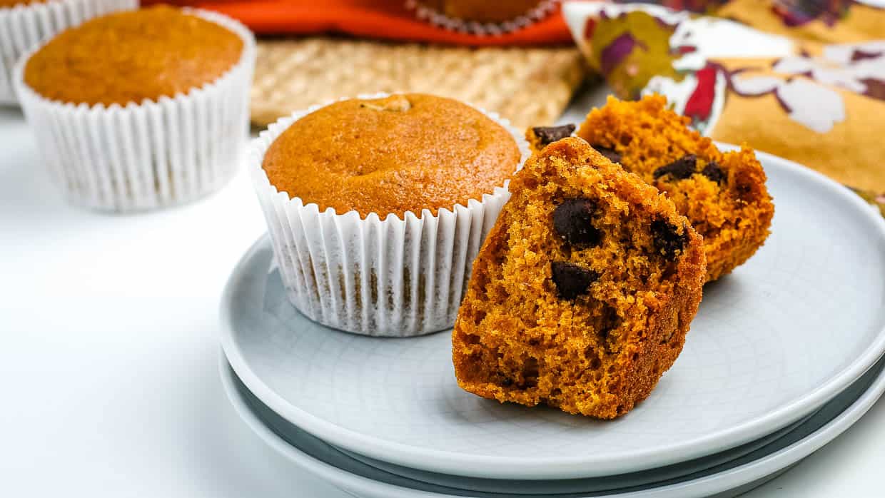 Chocolate chip pumpkin muffins on a plate with one cut open to show the insides.