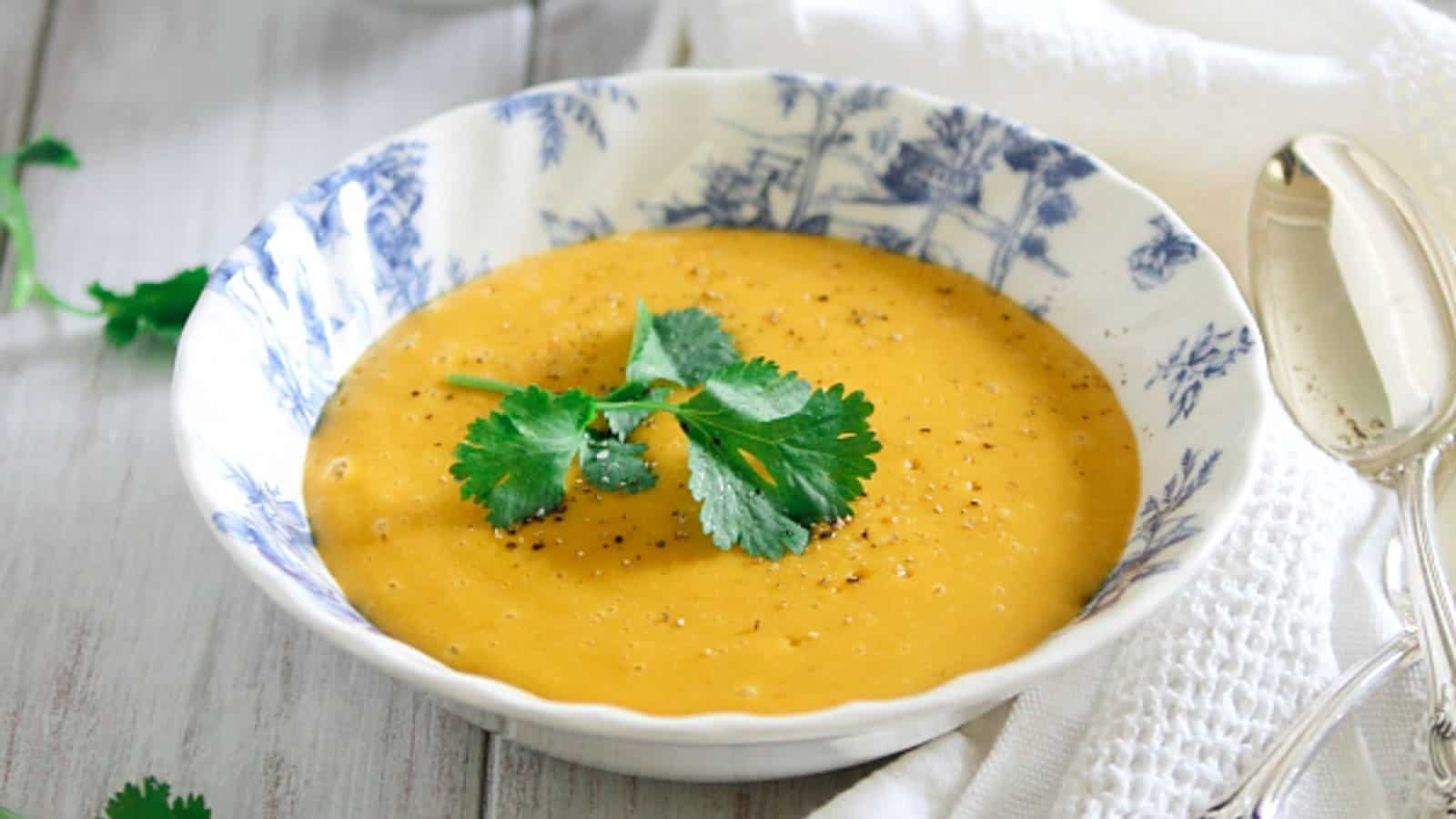 Pumpkin potato blender soup in a blue and white bowl garnished with fresh parsley.