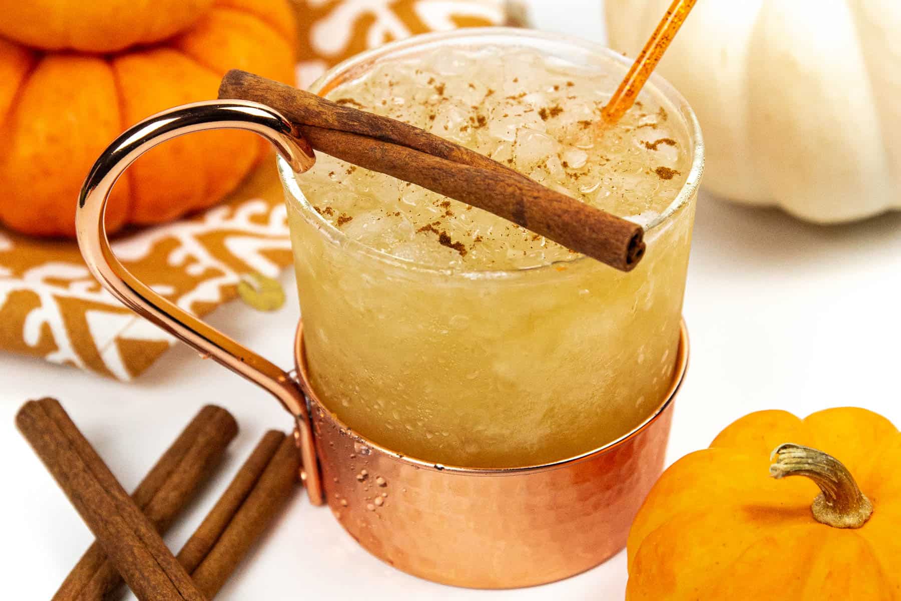 A drink with cinnamon sticks and pumpkins in a copper cup.