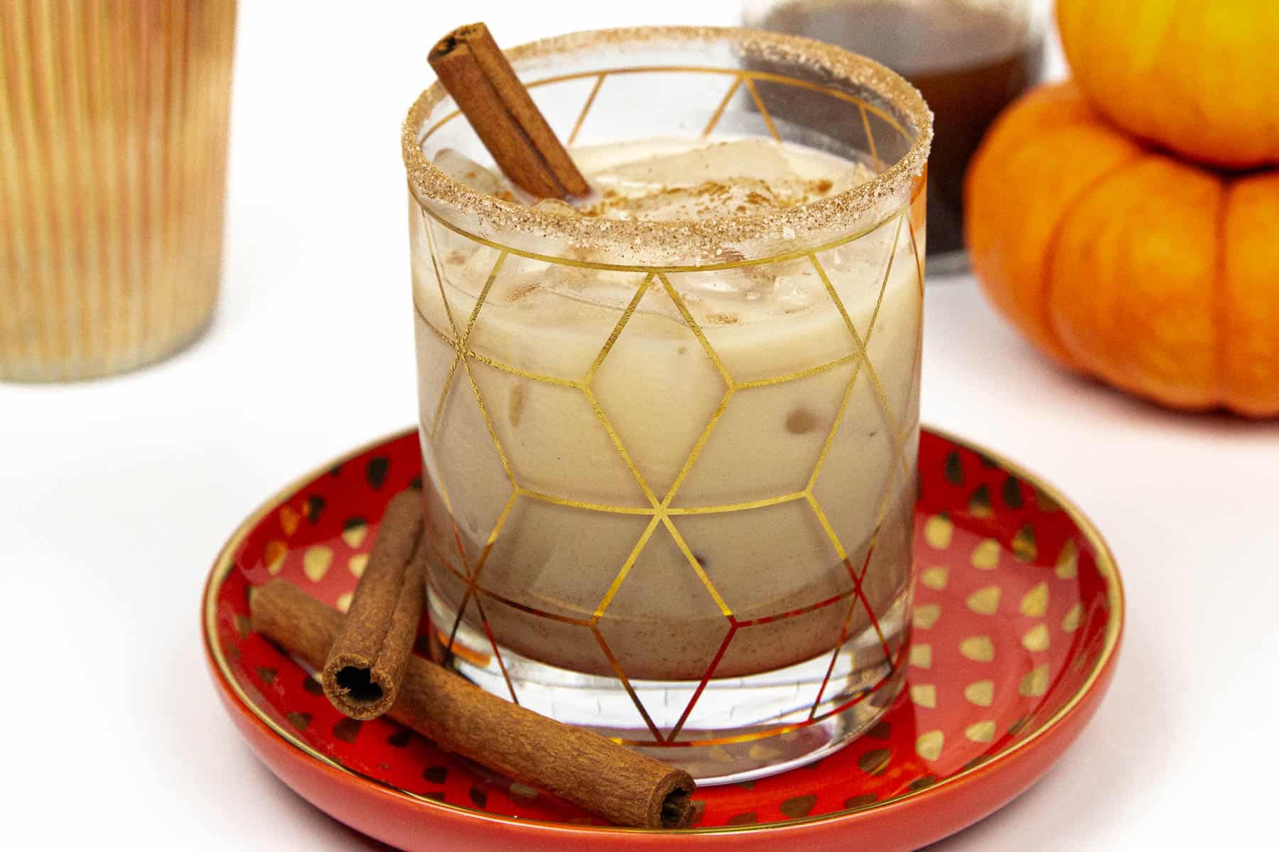A pumpkin spiced white russian on a plate with cinnamon sticks.