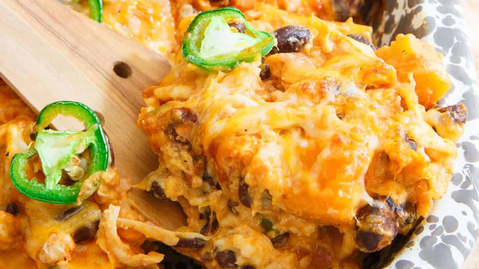 Pumpkin tortilla casserole in a baking dish with wooden serving spatula topped with jalapenos.