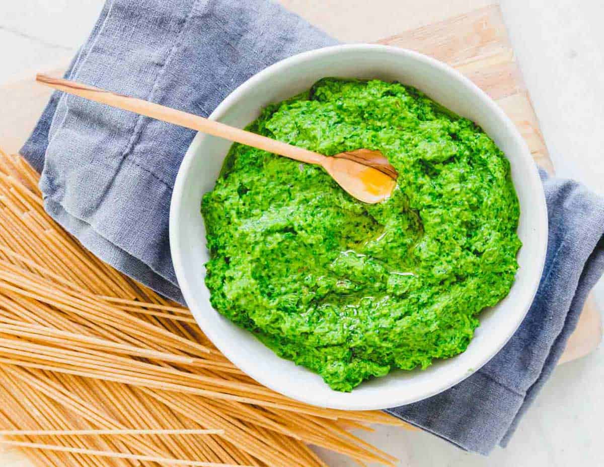 A bowl of ramp pesto with a wooden spoon and dried spaghetti to the side.