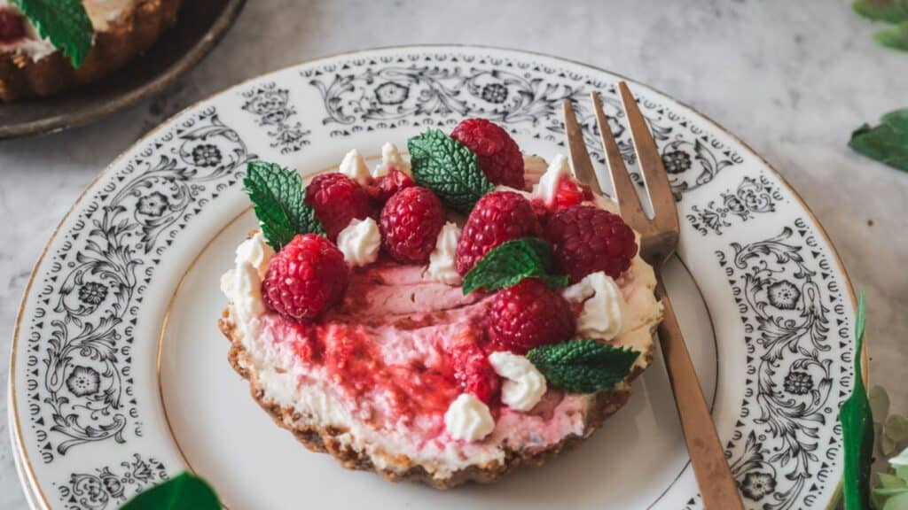 A plate with a raspberry cheesecake tart and a fork.