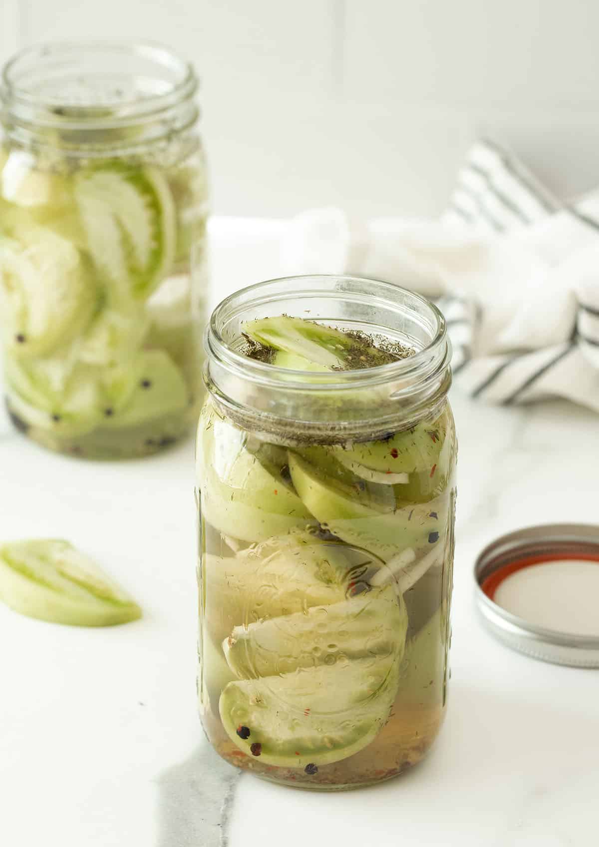 A large glass mason jar filled with pickled green tomatoes and onions. 