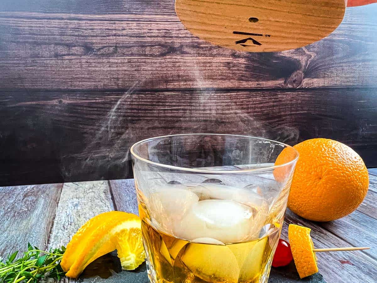 A glass of whiskey with oranges and a wooden stick.