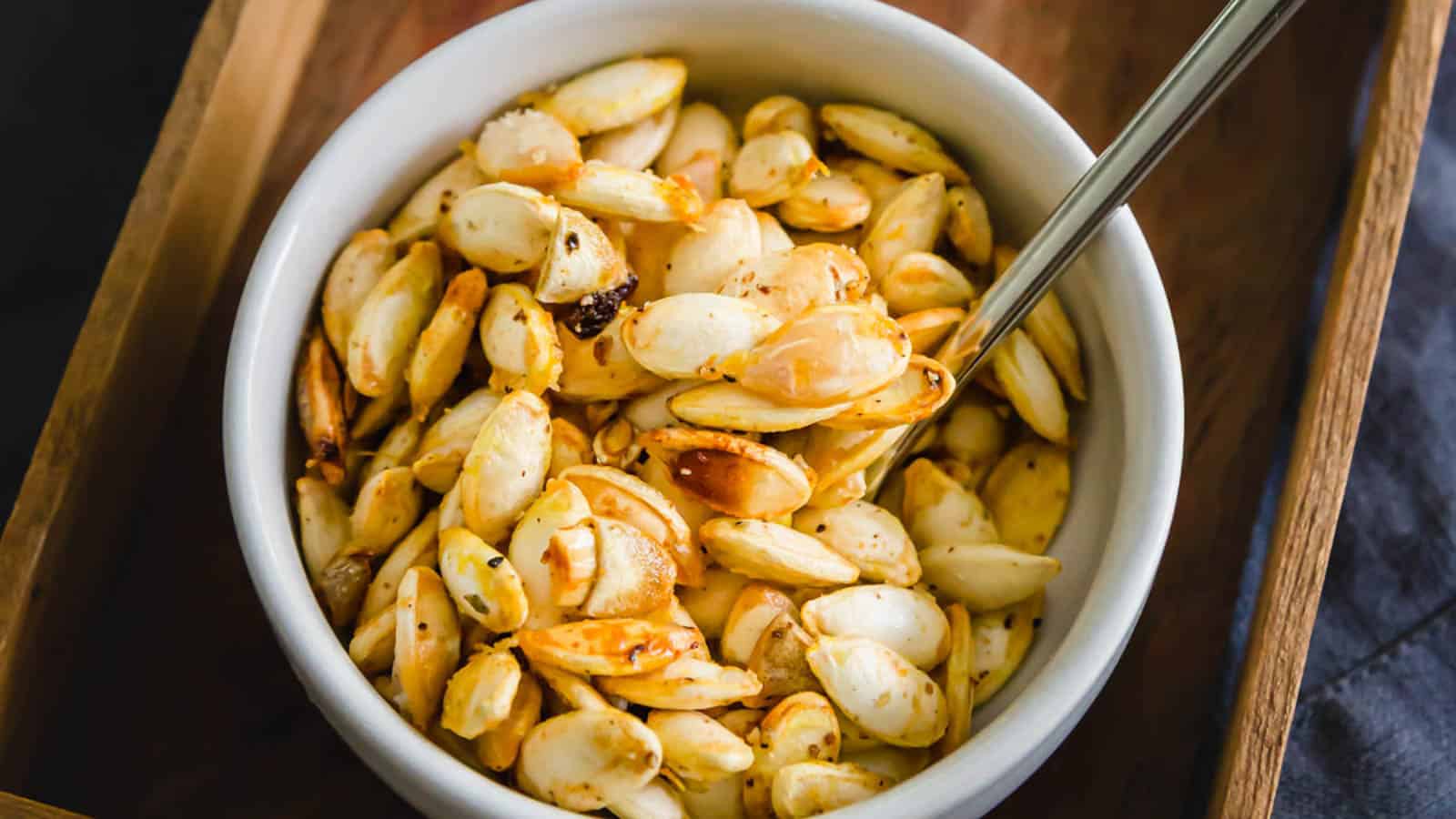 Roasted squash seeds in a white bowl with a spoon.