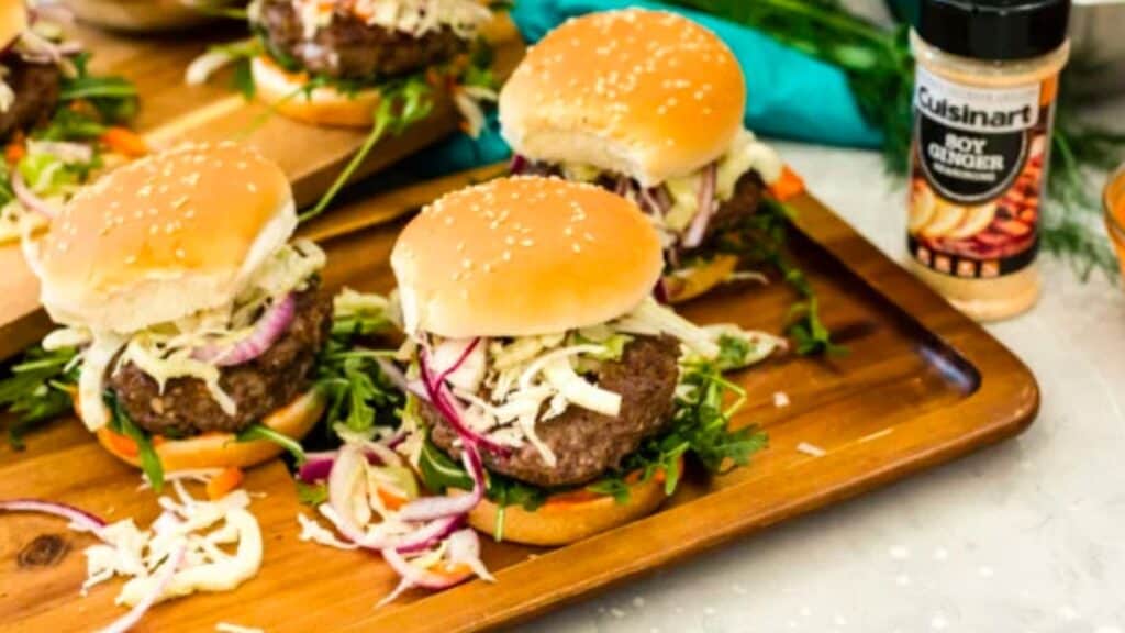 Burger sliders with coleslaw on a wooden cutting board.