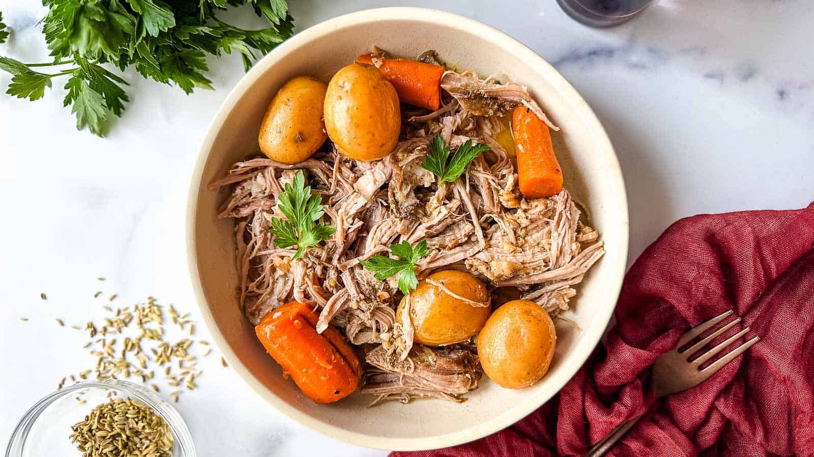 A white bowl with slow cooker Italian pork roast, potatoes and carrots.