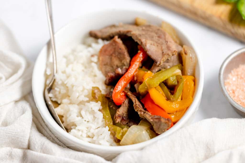 Beef stir fry with peppers and rice in a white bowl.