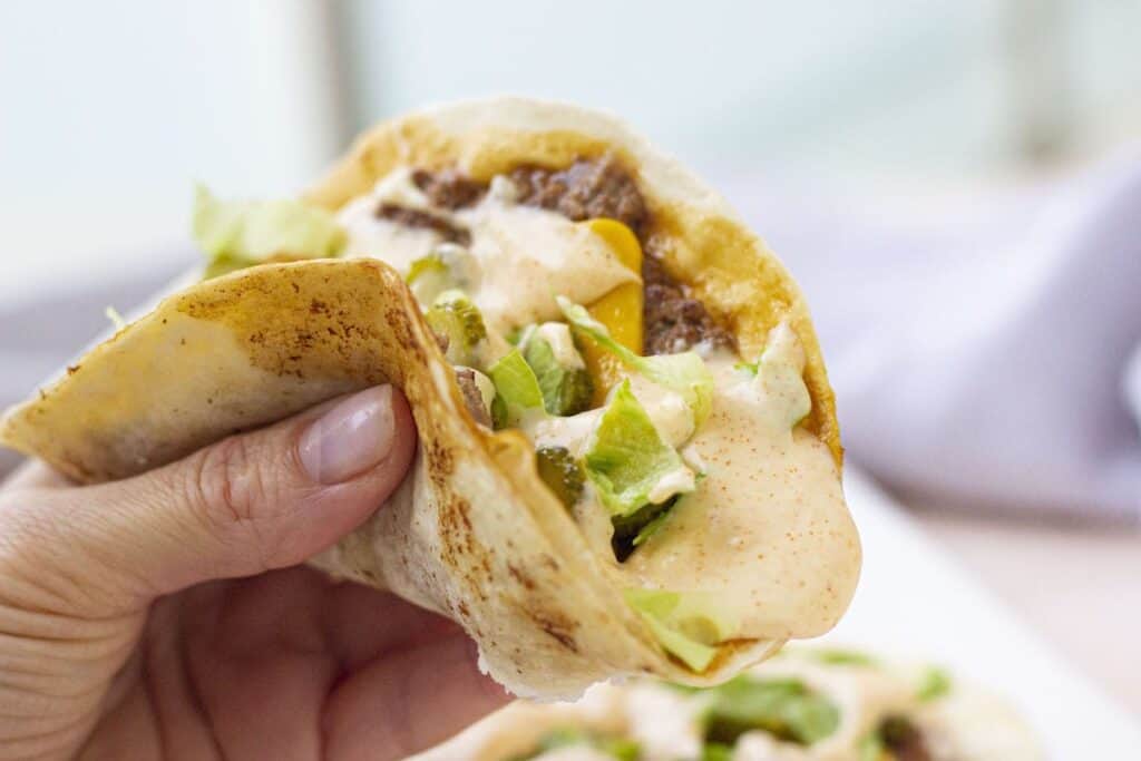 A person holding up a smash taco with lettuce and cheese.