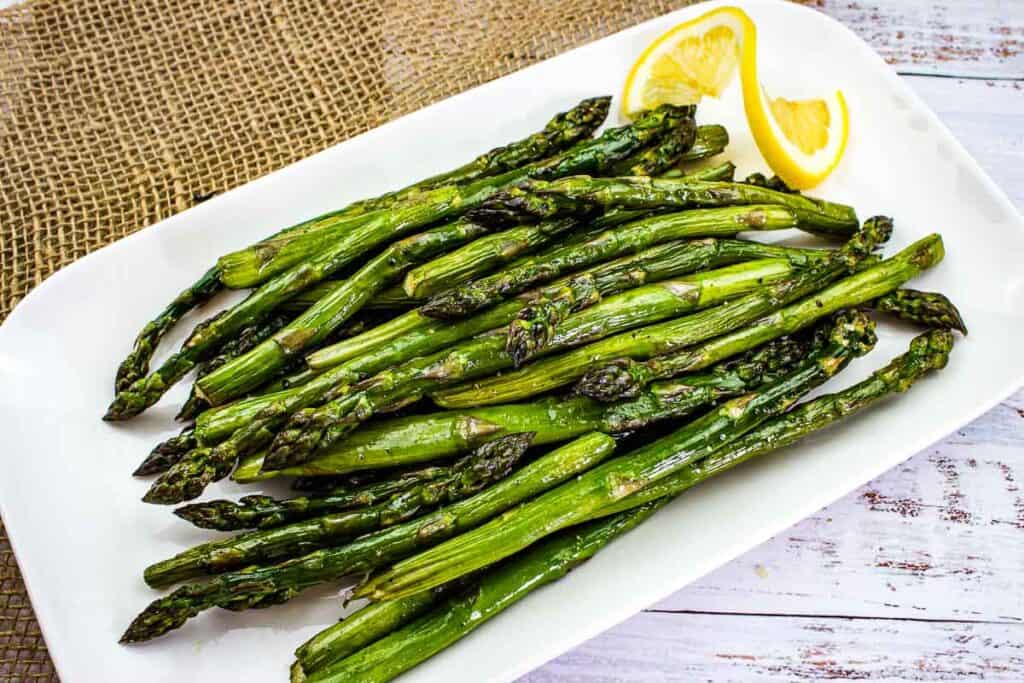 Smoked asparagus on a white plate with lemon wedges.