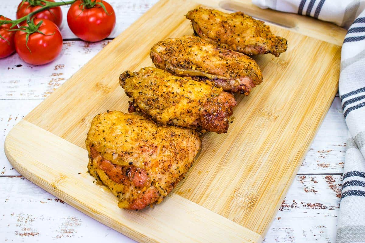 Chicken thighs on a cutting board with tomatoes.