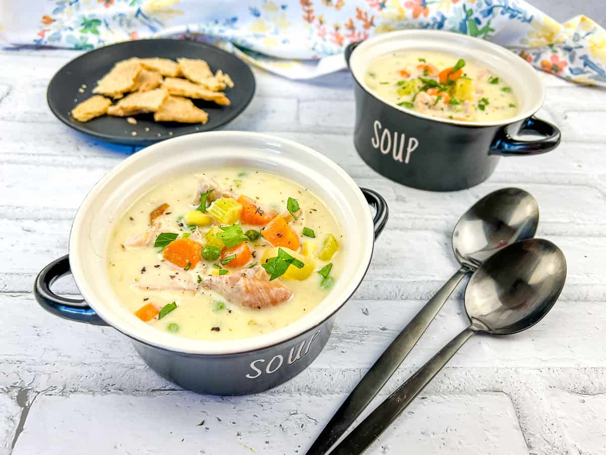 Two bowls of Turkey Pot Pie Soup with crackers and spoons.