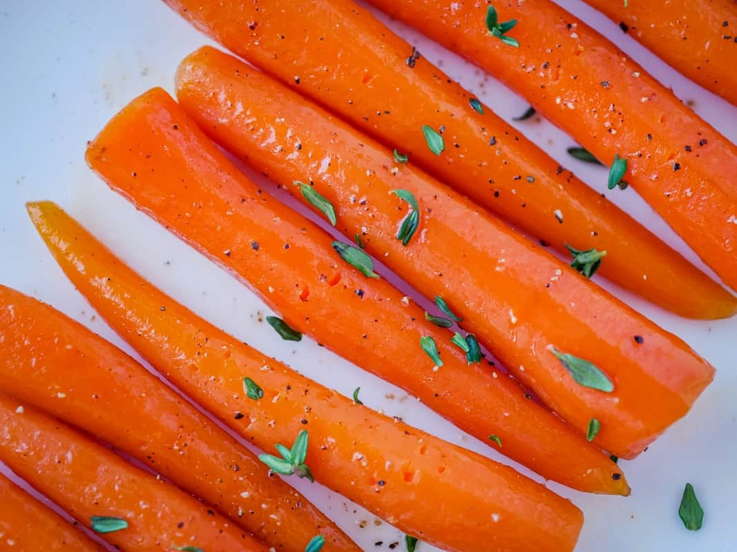 Carrots on a white plate with thyme sprigs.