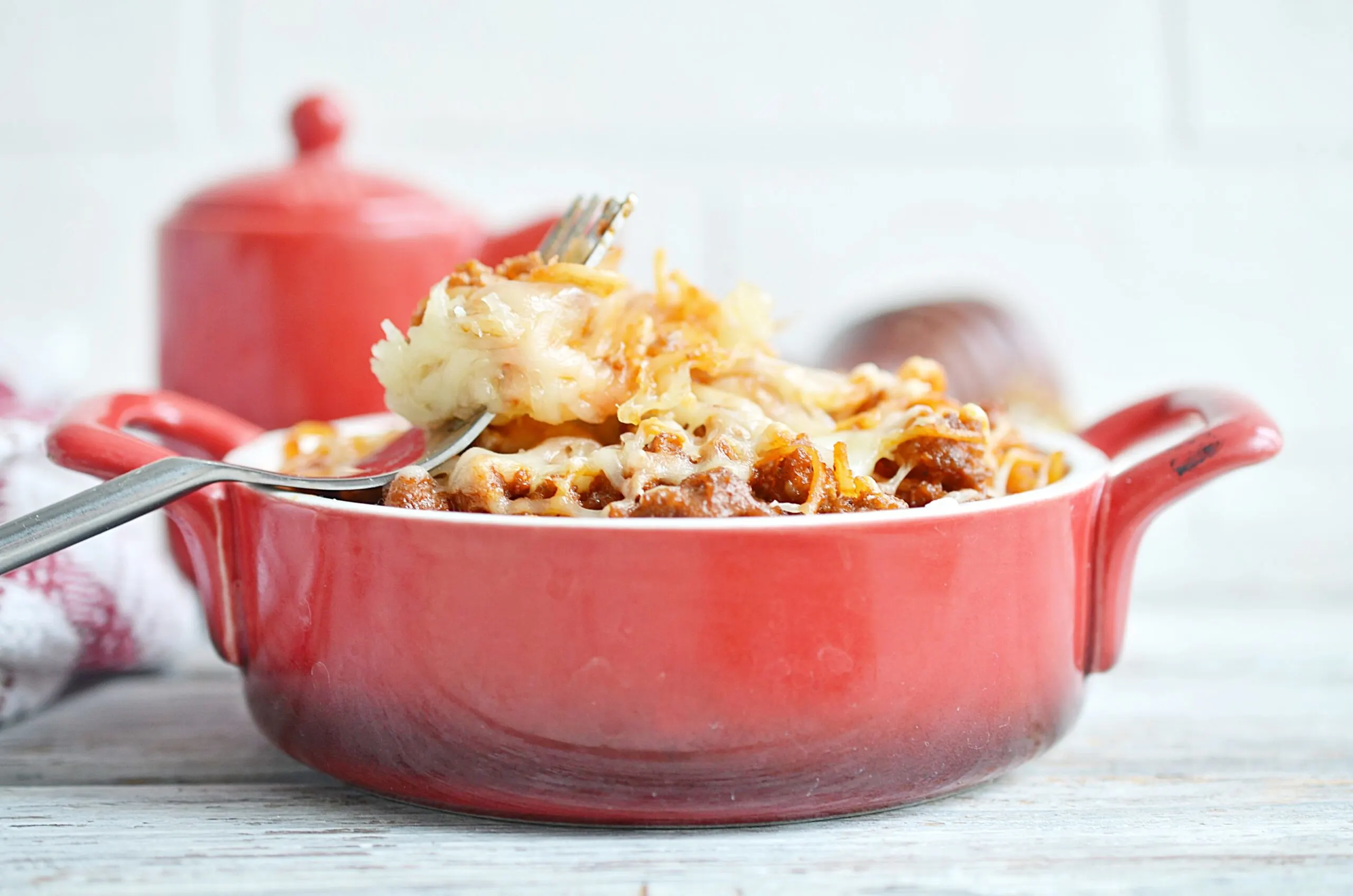 A red dish of spaghetti casserole with a fork in it, to the side.