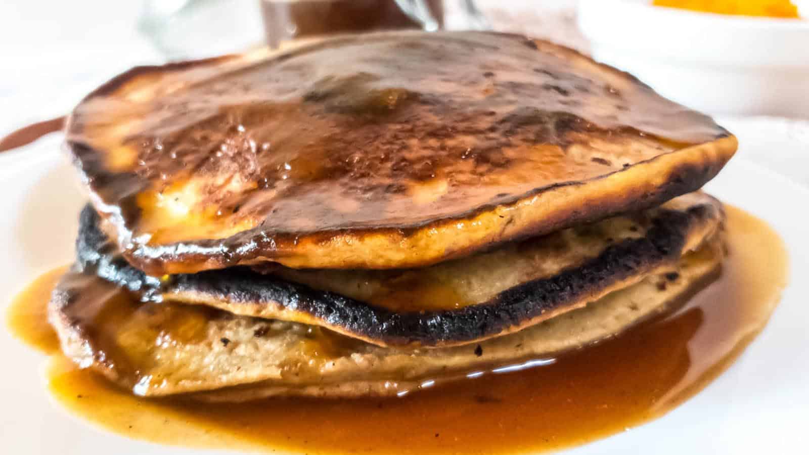 A stack of pancakes with pumpkin spice syrup on a plate.