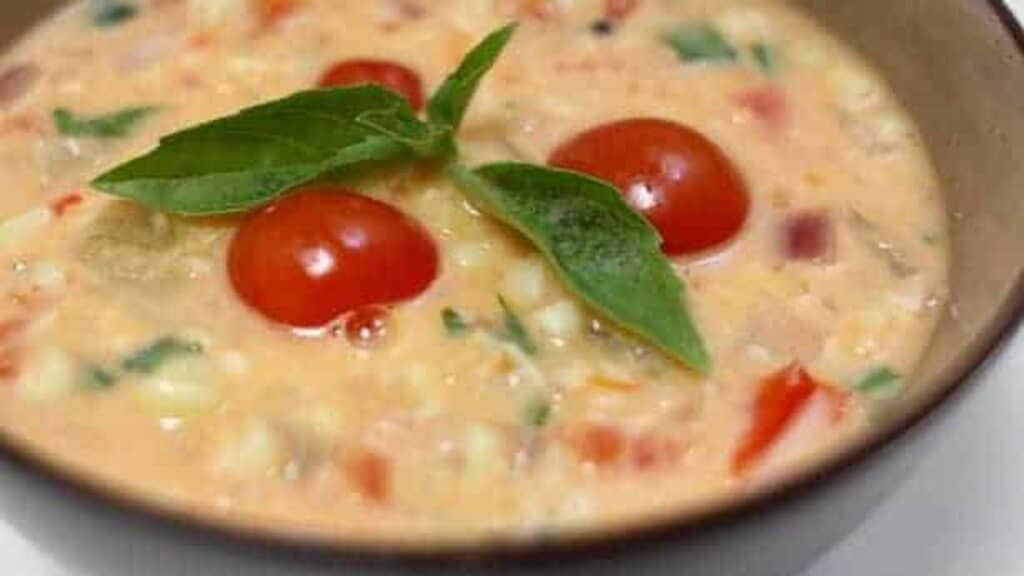 A bowl of corn chowder with tomatoes and basil.