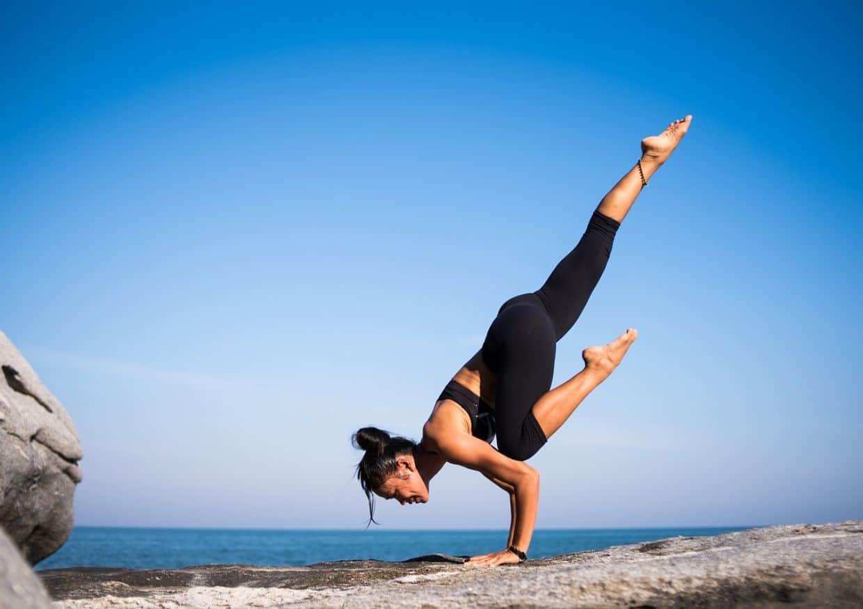 A woman is doing yoga on a rock in front of the ocean.