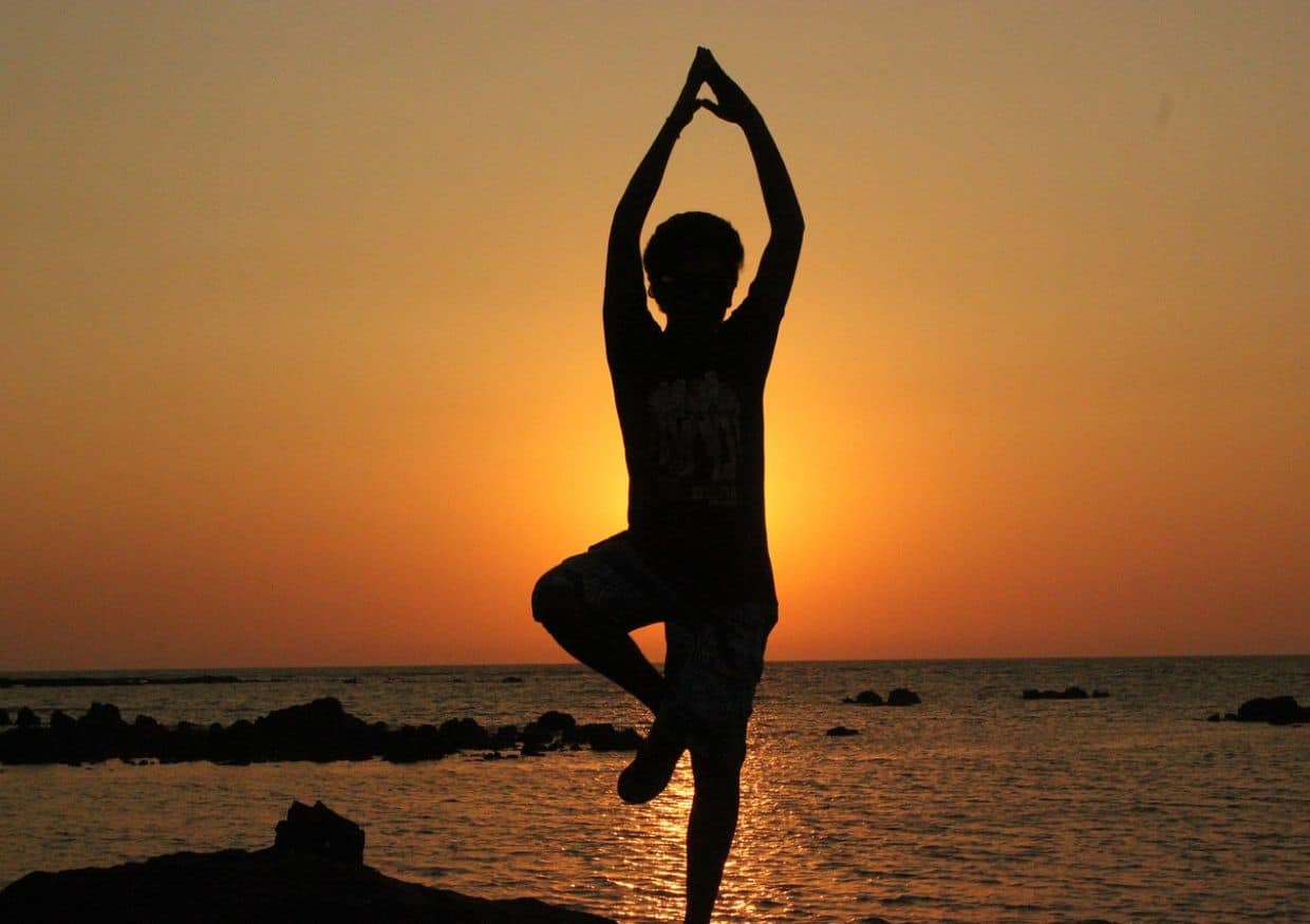 A silhouette of a person doing yoga on the beach at sunset.
