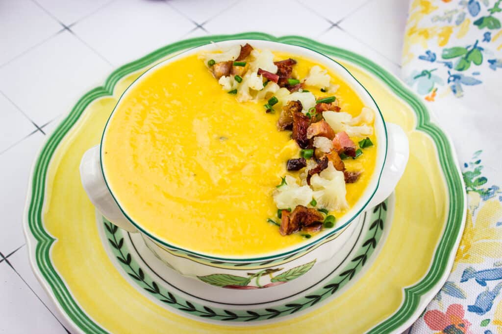 A bowl of Sweet Potato & Cauliflower Soup is sitting on a plate.